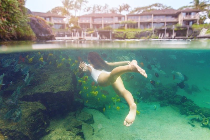 Woman swimming underwater with fish at King’s Pond (Four Seasons Hualalai on the Big Island)