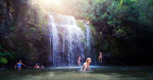 Swimmers in the pool below a wide waterfall in North Kohala
