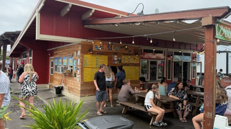 Customers ordering at the Kula Shave Ice kiosk in Hilo, with a burgers and fries stand and picnic tables alongside