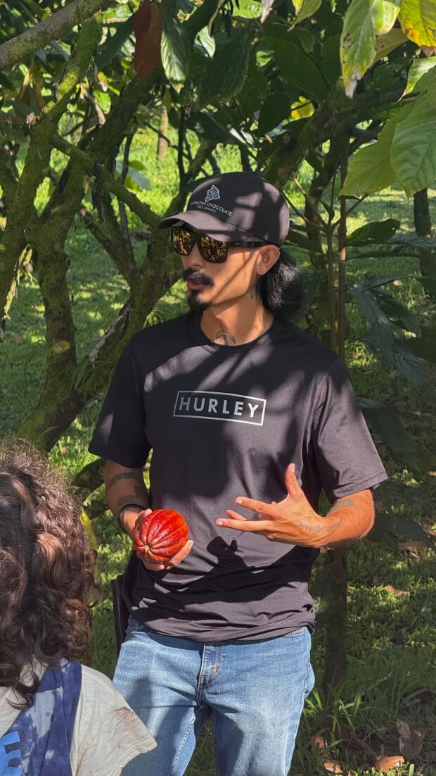 Tour guide holding a ripe cacao pod and explaining to visitors in the orchard at Lavaloha Farm, Hilo, Hawaii