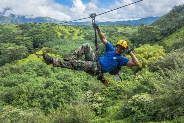 Zipliner leaning back upside-down style while gliding over the rainforest canopy on Kauai
