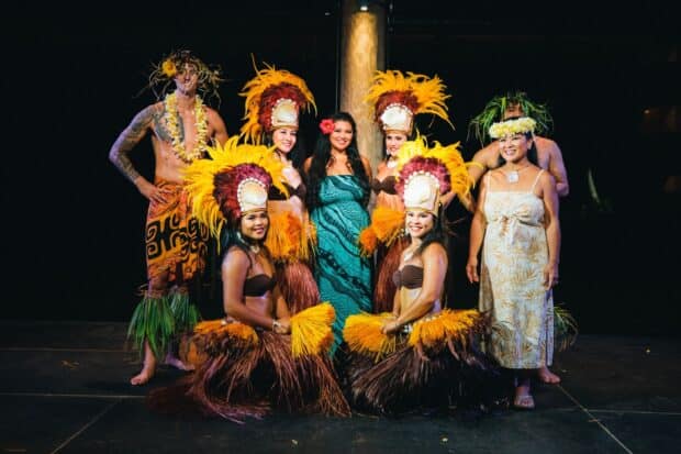 Lūʻau Ka Hikina cast in Tahitian feather headdresses and costumes posing together on the stage