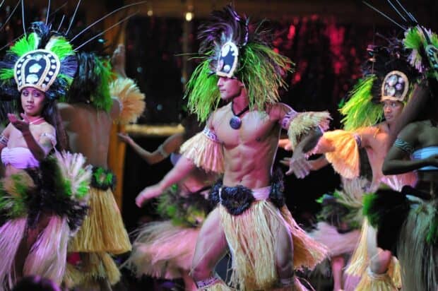 Tahitian dancers in feathered shell headdresses and grass skirts perform in the Luau Kalamaku show on Kauaʻi