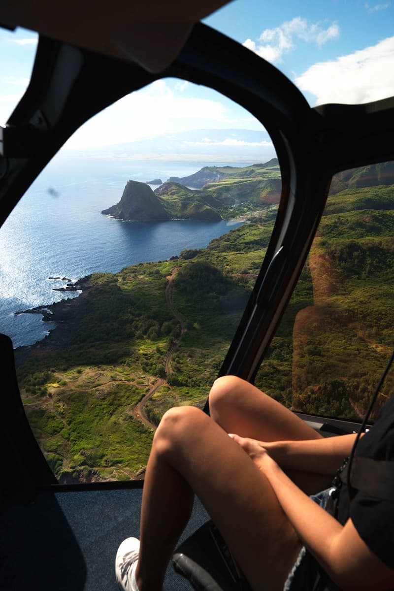 woman sitting in A helicopter crossing the Maui coastline with Haleakala on the horizon