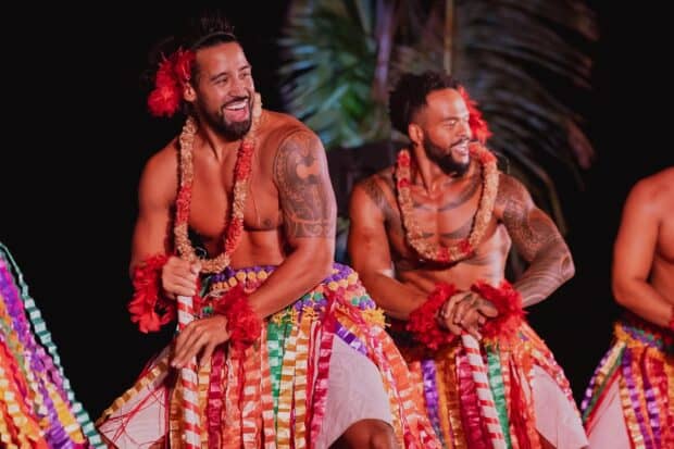 Two male dancers in ribbon skirts and red feather cuffs perform at night at the Mauka Warriors Luau in Kapolei