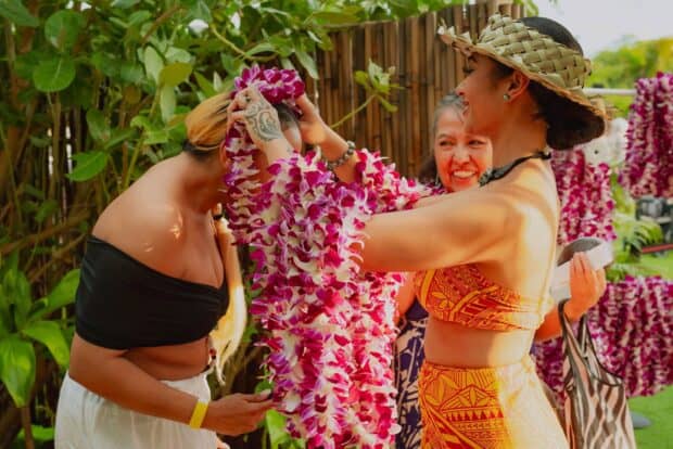 A staff member places an orchid lei over a guest's head at check-in for the Mauka Warriors Luau in Kapolei