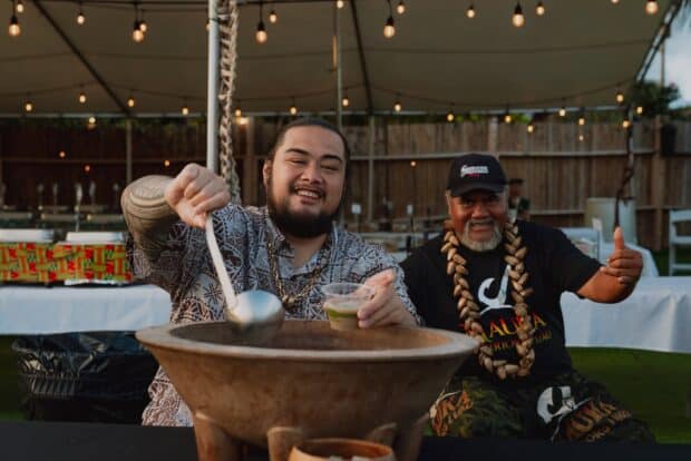 A server ladles kava from a large carved wooden bowl and hands a cup to a guest at the Mauka Warriors Luau in Kapolei
