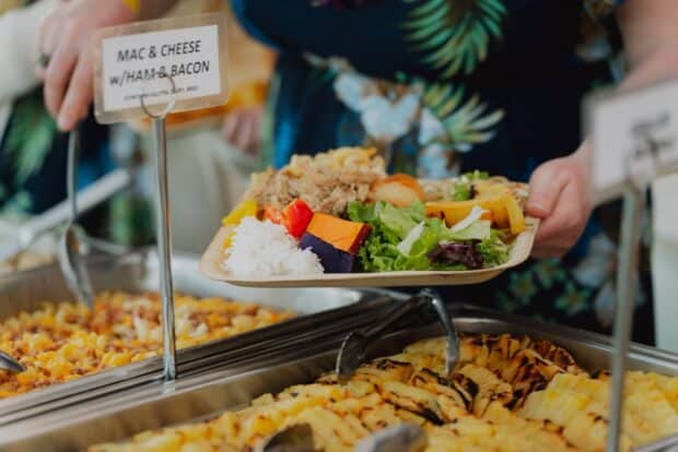 Palm-leaf plate with kālua pork, rice, purple sweet potato, salad, and grilled pineapple at the Mauka Warriors Luau buffet