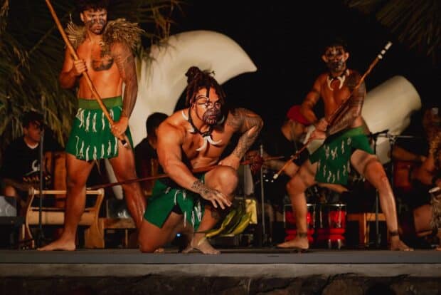Three performers with painted faces and wooden spears on stage at the Mauka Warriors Luau in Kapolei