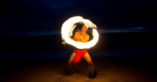 Fire performer spinning a ring of fire on the beach at night at Huakaʻi Lūʻau, Maui