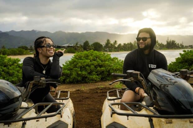 Two riders laughing on their ATVs beside the ocean at North Shore Stables in Waialua