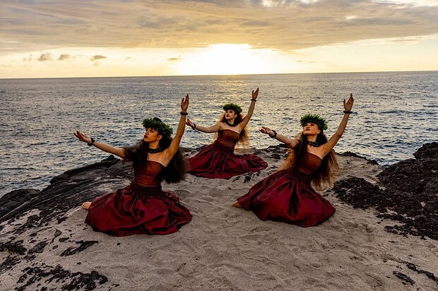 Three dancers on the beach with sunset behind them
