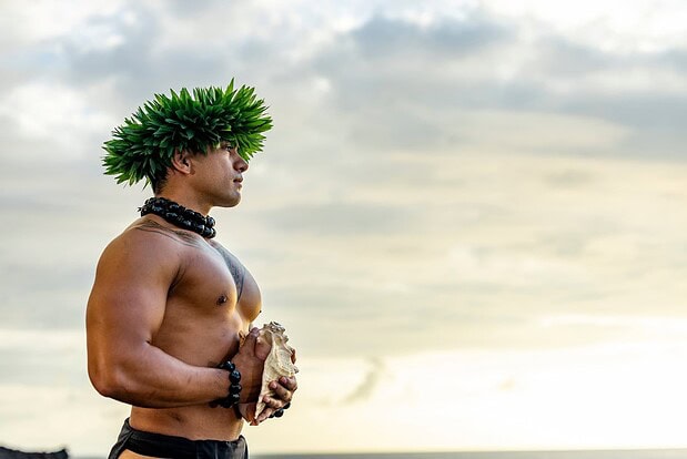 Man in traditional headdress holding a pū (conch shell horn)