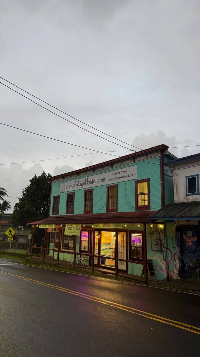 Teal historic building on Pāhoa's main street at dusk, home to the Pahoa Village Hostel above The Veli deli