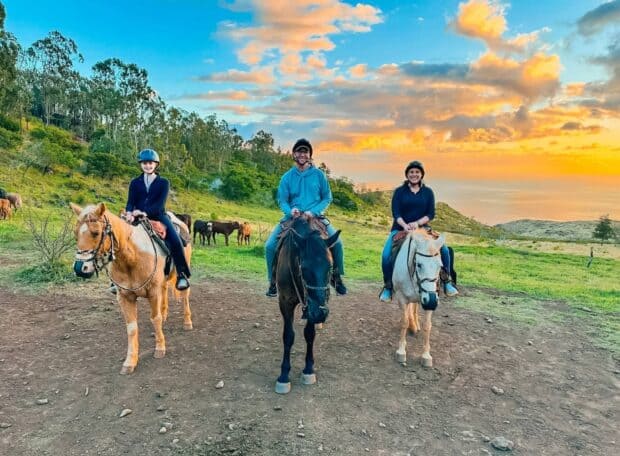 Three riders on horseback at sunset on the Pālehua mountain trail above the West Oʻahu coast