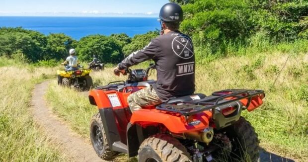 Line of solo ATV riders crossing open grassland with ocean views on the Big Island ATV tour near Kona