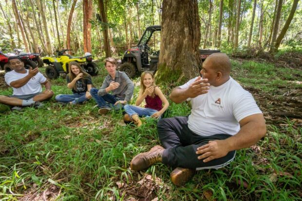 Group seated in a circle while a Polynesian guide leads a hands-on cultural activity at a village stop, Aloha Adventure Farms ATV tour