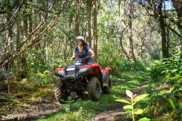 Woman smiling while riding solo ATV through forested trail on the Polynesian Cultural ATV tour at Aloha Adventure Farms