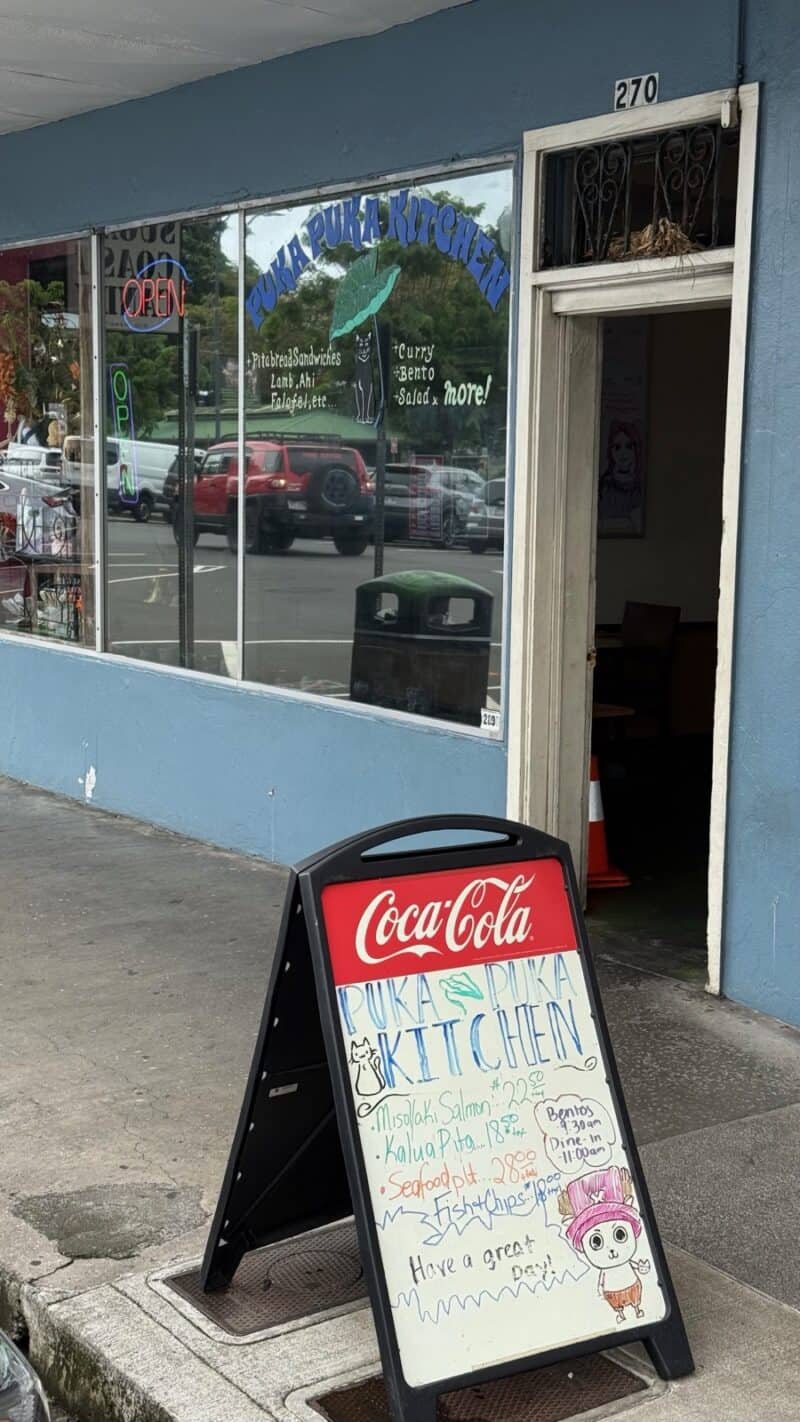 Hand-lettered sidewalk menu board outside Puka Puka Kitchen in Hilo, listing bentos and plate specials