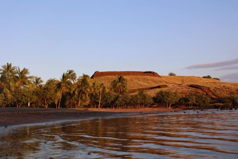 Stone walls of Puʻukoholā Heiau on the hillside above Pelekane Bay at sunset