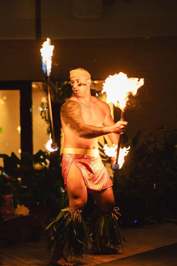 Fire knife dancer spinning two lit torches on the wooden stage at Queens Waikiki Luau