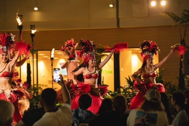 Tahitian dancers in red feather headdresses and raffia skirts on stage at Queens Waikiki Luau