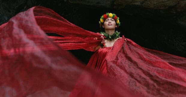 A dancer in flowing red fabric and a flower haku lei performs at the Kapa Moe Lūʻau