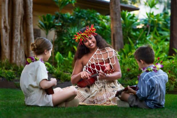 A performer gives keiki a ukulele lesson on the lawn before the Kapa Moe Lūʻau