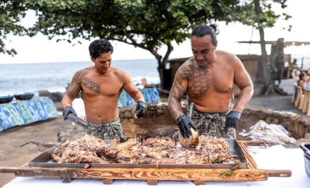 Two Hawaiian practitioners prepare roasted pork from the imu at the Royal Kona Luau.