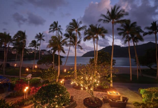 Palm trees and lit garden paths at the Royal Sonesta Kauaʻi lead down to Kalapaki Beach and the bay at dusk