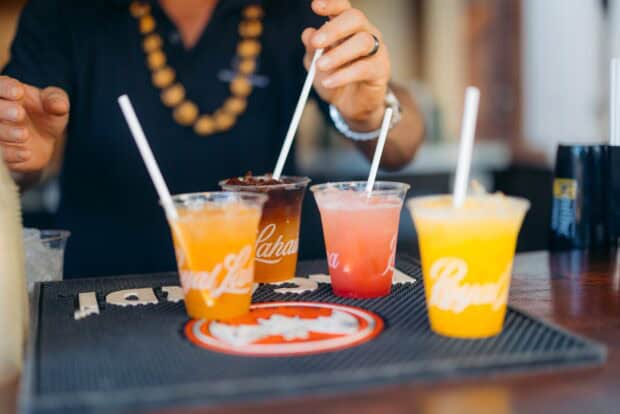 Four tropical drinks in Royal Lahaina cups on a bar mat with a server behind
