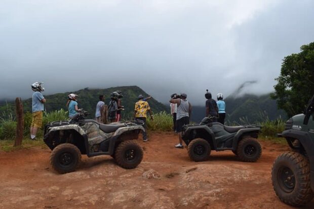 roup of ATV riders dismounted at a misty mountain overlook with their quads parked on red dirt