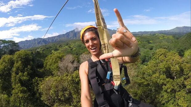 Zipliner throwing a shaka while gliding across a valley framed by Kauai's green mountains