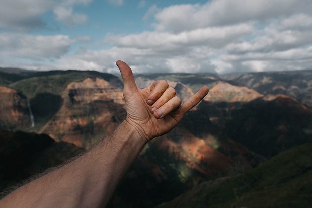 hand trowing shaka signal against mountains in background