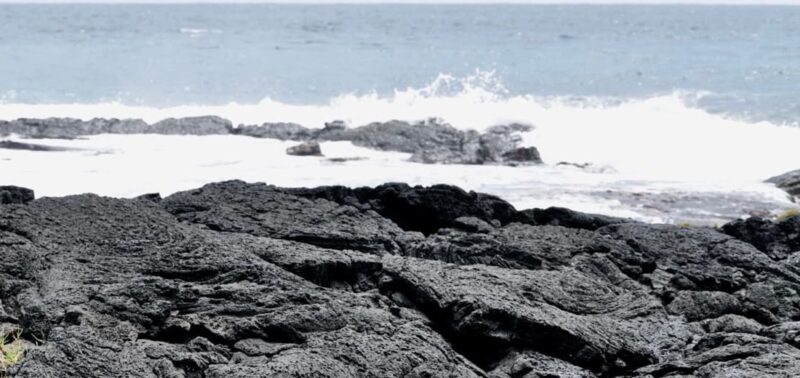 Dark lava shelf at the shoreline with surf breaking over a low ledge and open sea beyond
