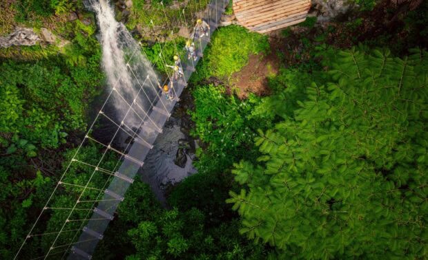 Aerial view of a suspension sky bridge crossing a gulch beside a waterfall, guests walking across