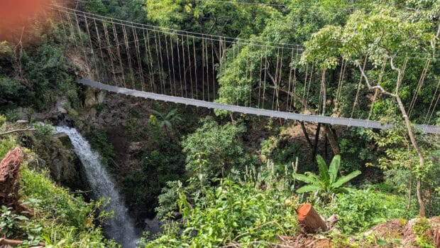Suspension sky bridge crossing a gulch alongside a waterfall in North Kohala