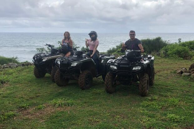 Three ATV riders posing on their quads on a grassy clearing above the Pacific on an overcast day