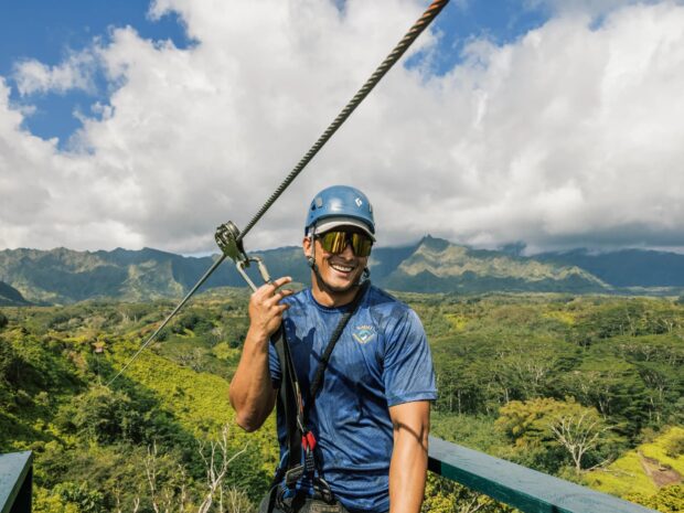 Smiling man standing on a zipline platform, clipped in and ready to launch on the Kauai Backcountry tour