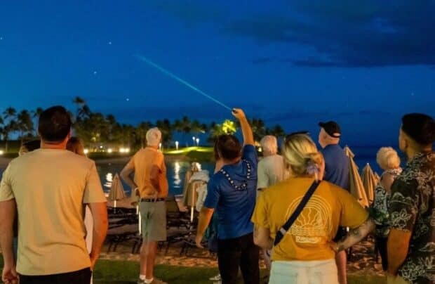 Astronomer pointing a green laser at the darkening sky for a group of guests at a Stars Above Hawaii star show on Oʻahu
