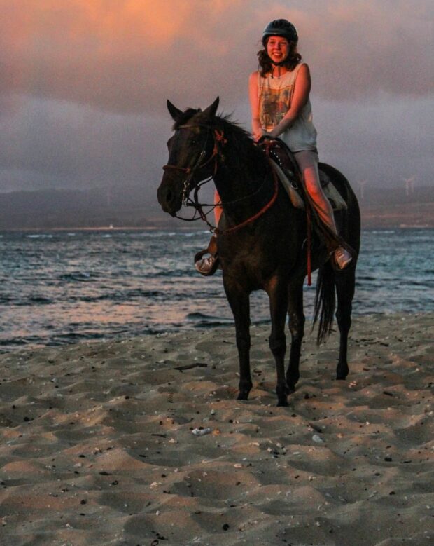 Woman standing with polo pony on Mokuleia Beach at sunset, Oʻahu North Shore
