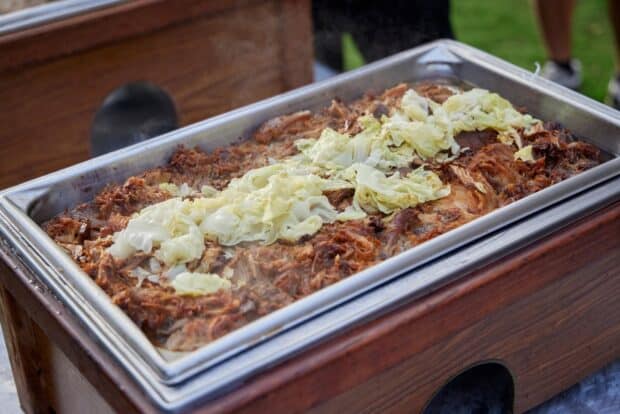 Shredded kālua pig with steamed cabbage in a stainless pan set into a wooden chafing box