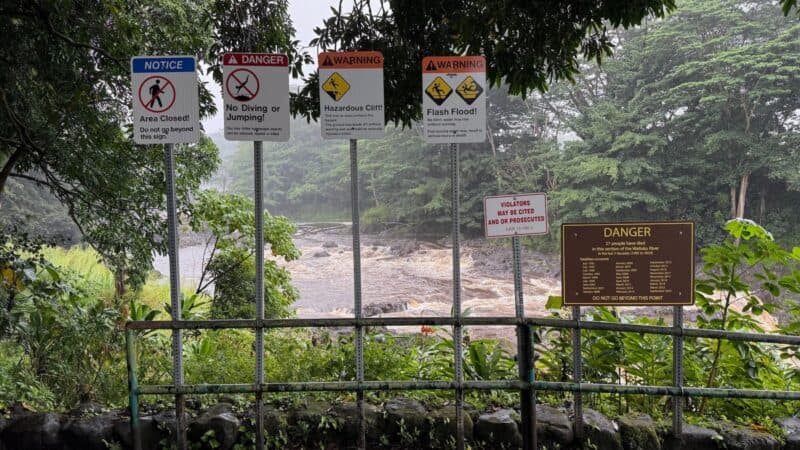 Row of warning signs at Rainbow Falls: area closed, no diving or jumping, hazardous cliff, and flash flood
