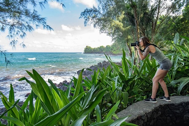 Visitor photographing the ocean from a lookout at the Hawaii Tropical Botanical Garden