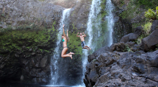 people jumping in water next to waterfall